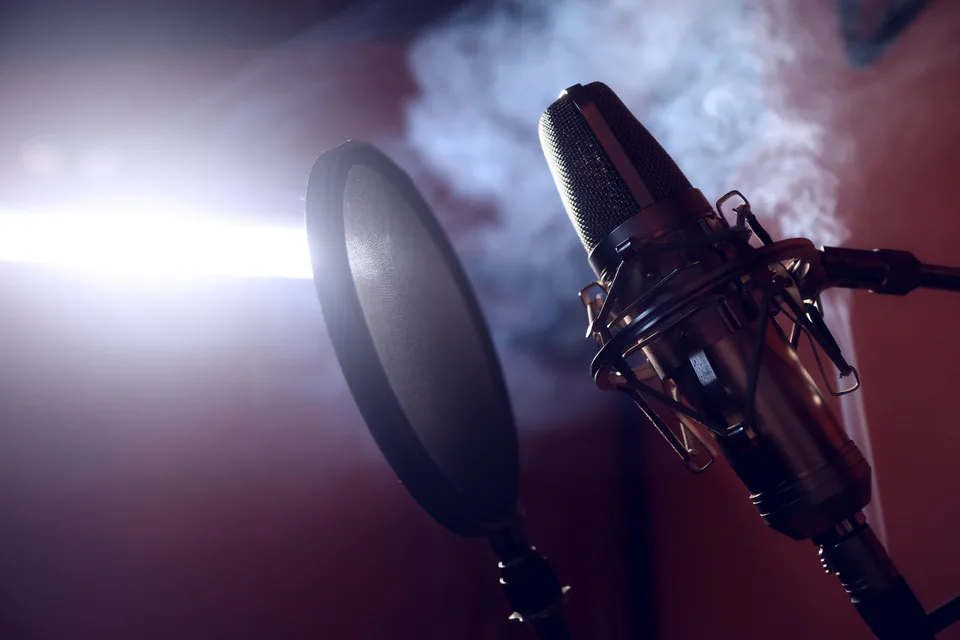 A studio condenser microphone with a pop filter lit dramatically in a dark room